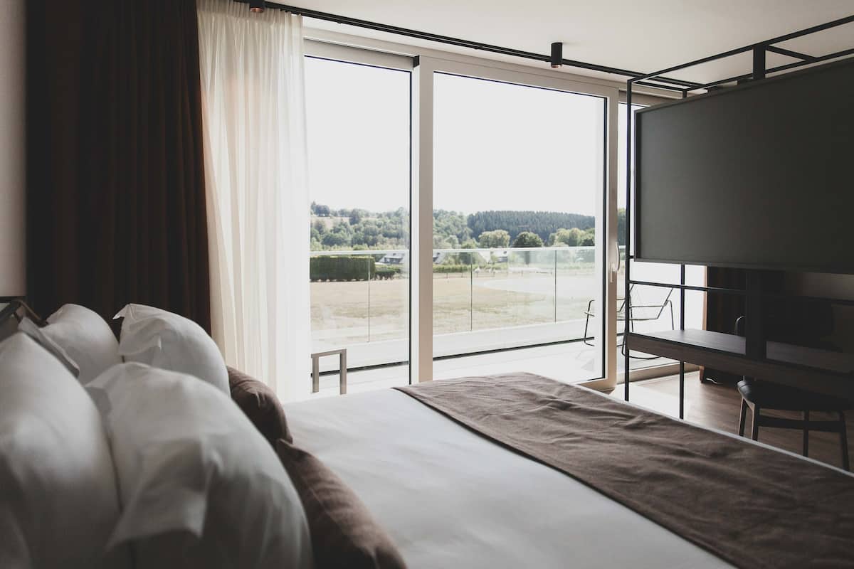 A hotel room with a large bed, a TV, and a balcony with a view of a lake and trees.