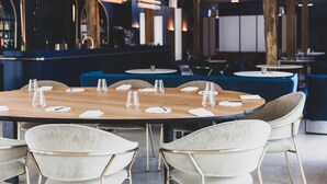 A restaurant with round tables set for dining, white chairs, and a bar area in the background. - Roannay – Francorchamps (Stavelot)