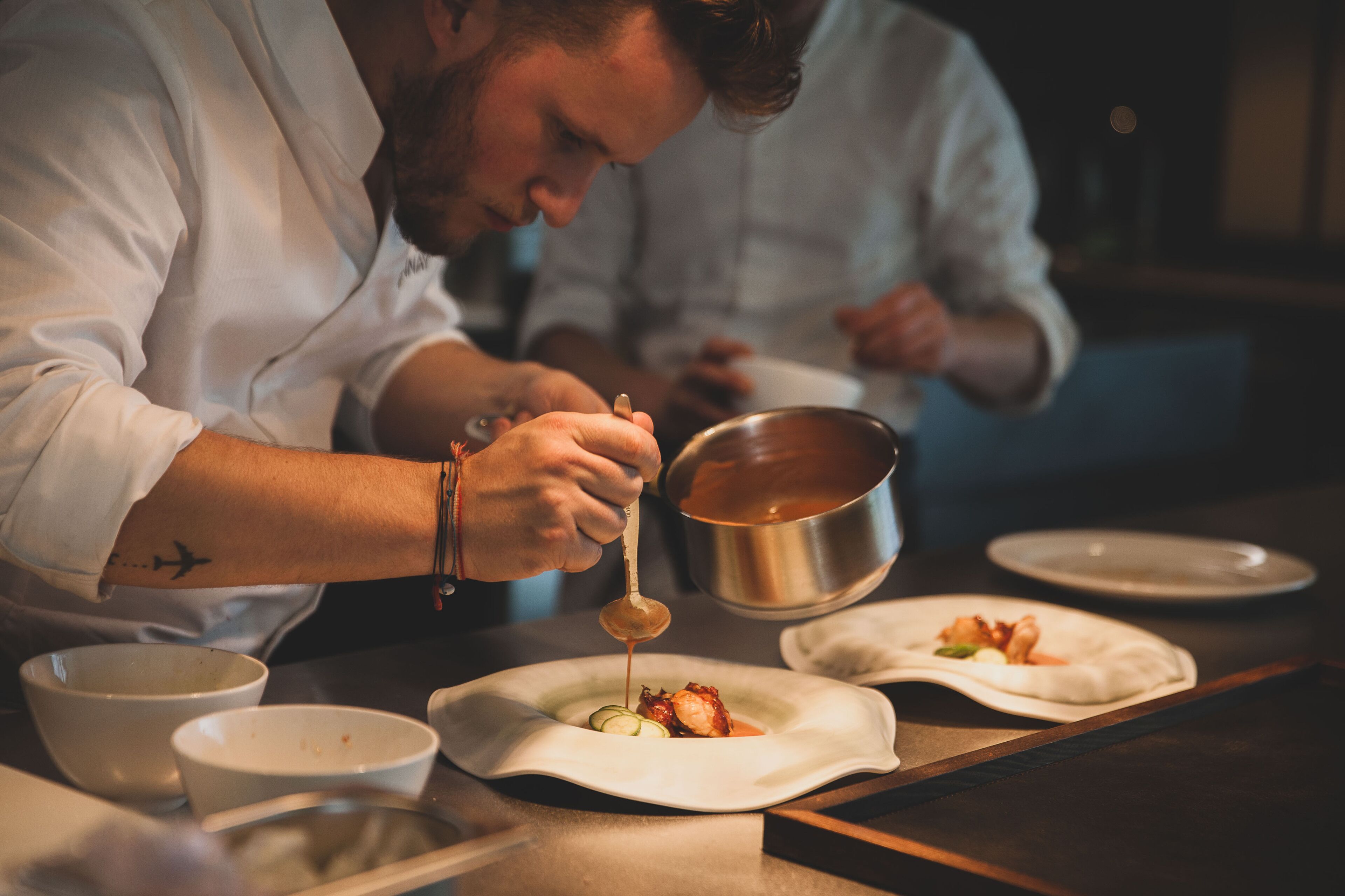 Un chef vertiendo salsa sobre un plato.