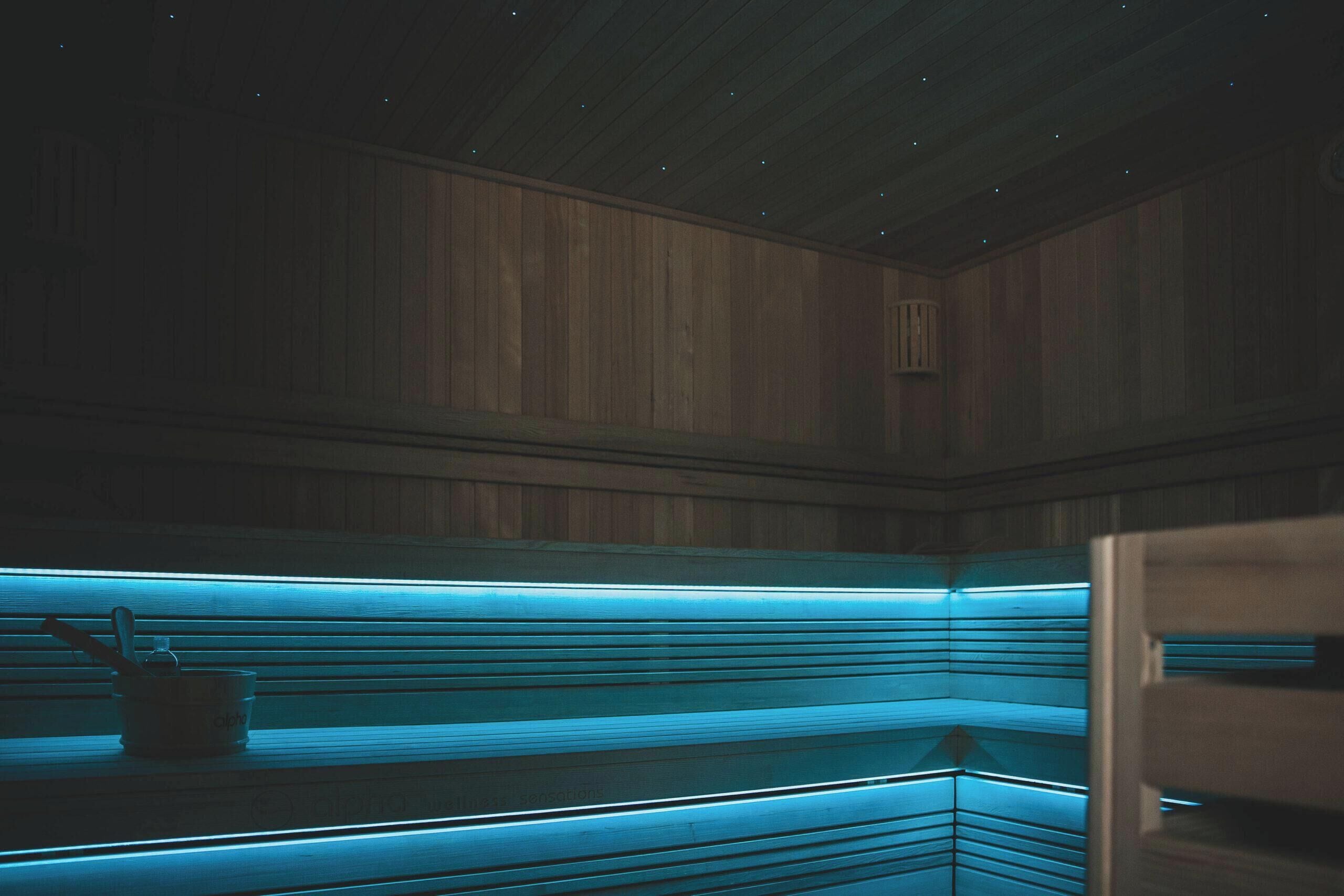 A sauna with wooden walls and benches, illuminated by blue lighting.