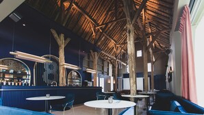 A restaurant with high wooden beams, round tables, and blue seating. - Roannay – Francorchamps (Stavelot)