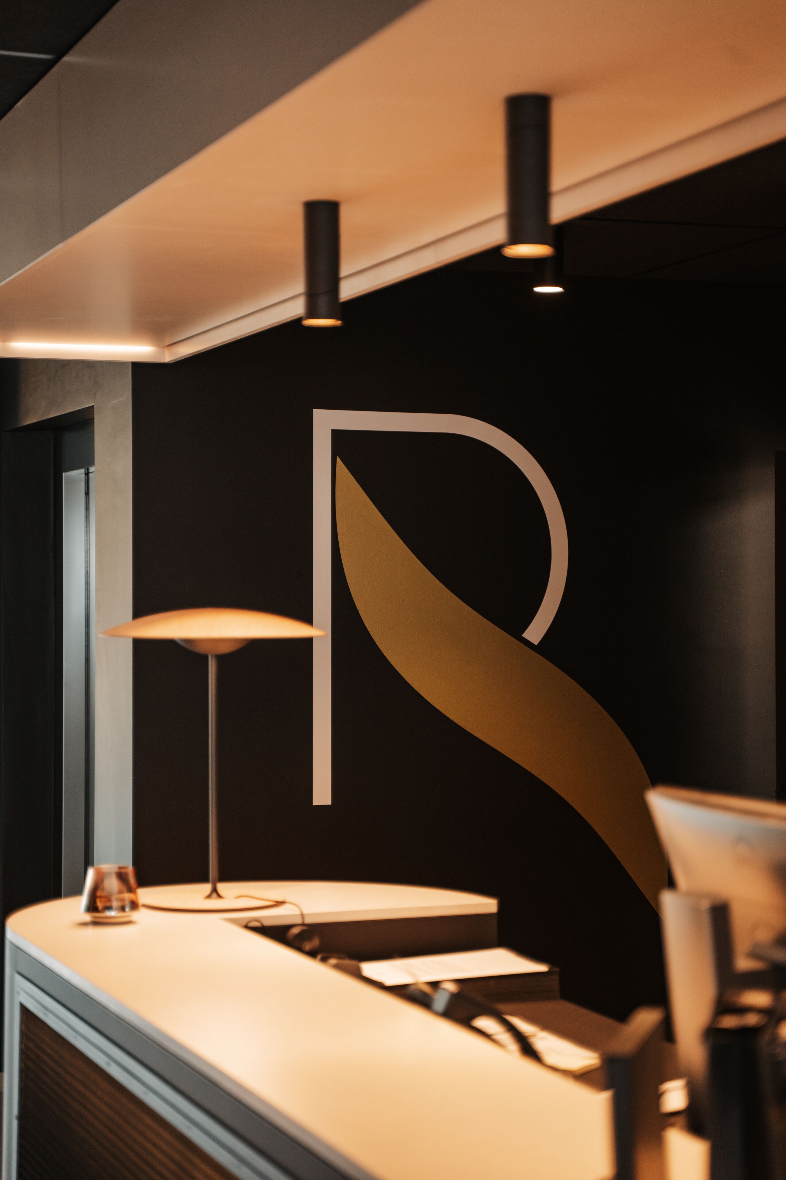 Un comptoir d’accueil moderne au design minimaliste, agrémenté d’un grand logo abstrait sur le mur qui le surplombe.