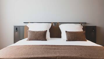 A neatly made bed with a brown blanket and two pillows, a headboard, and a wall-mounted shelf.