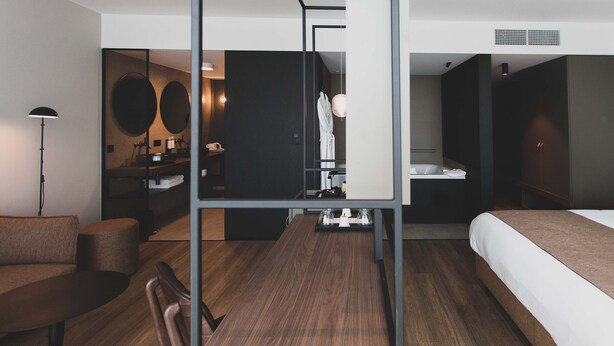 A modern hotel room with a wooden floor, a bed, a sofa, a desk, and a mirror. - Roannay – Francorchamps (Stavelot)