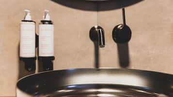 A bathroom with a black sink, two bottles of Clarins body lotion, and a black faucet.
