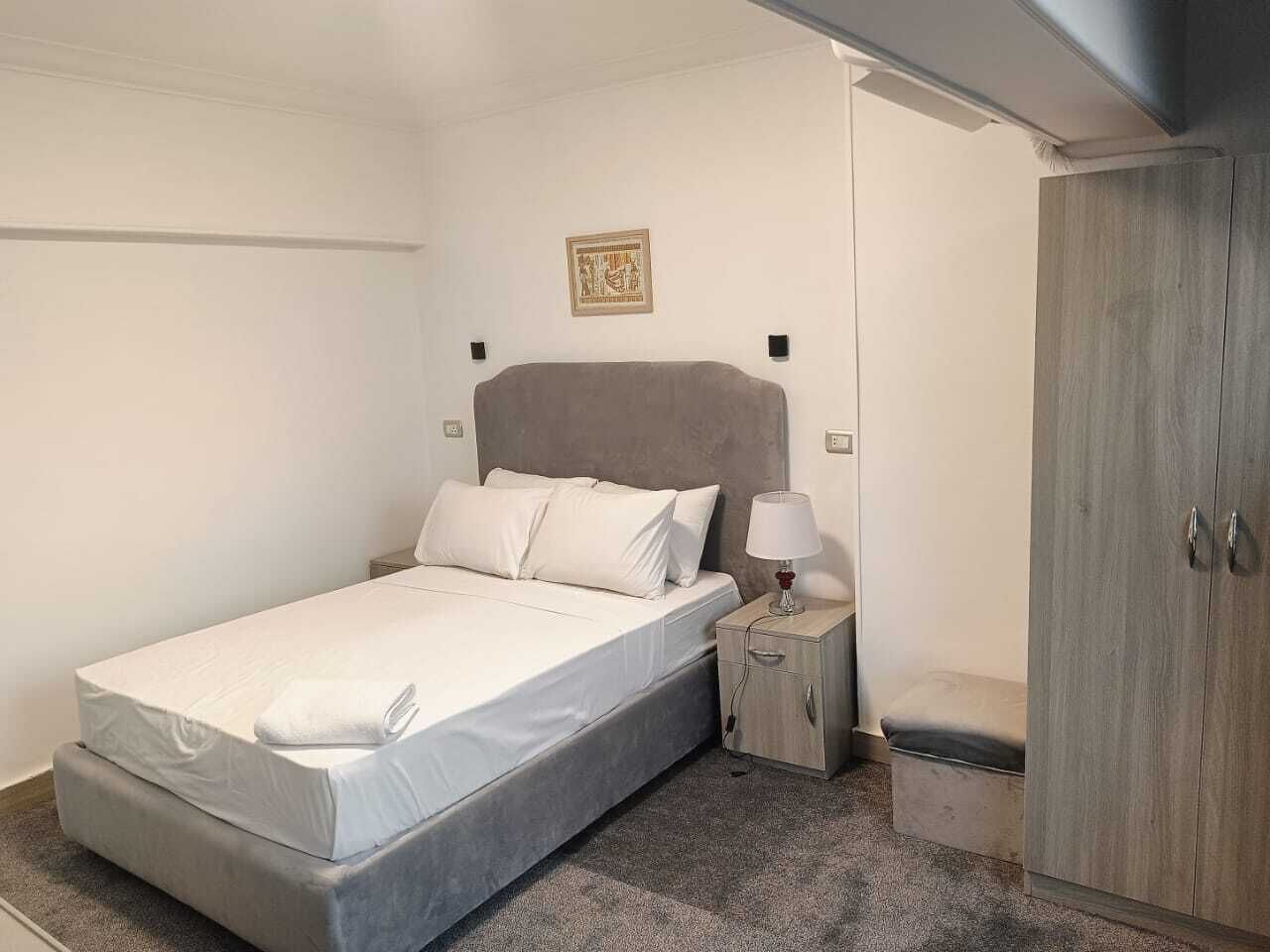 Ein Einzelbett mit grauem Kopfteil, ein Nachttisch mit Lampe und ein Kleiderschrank.