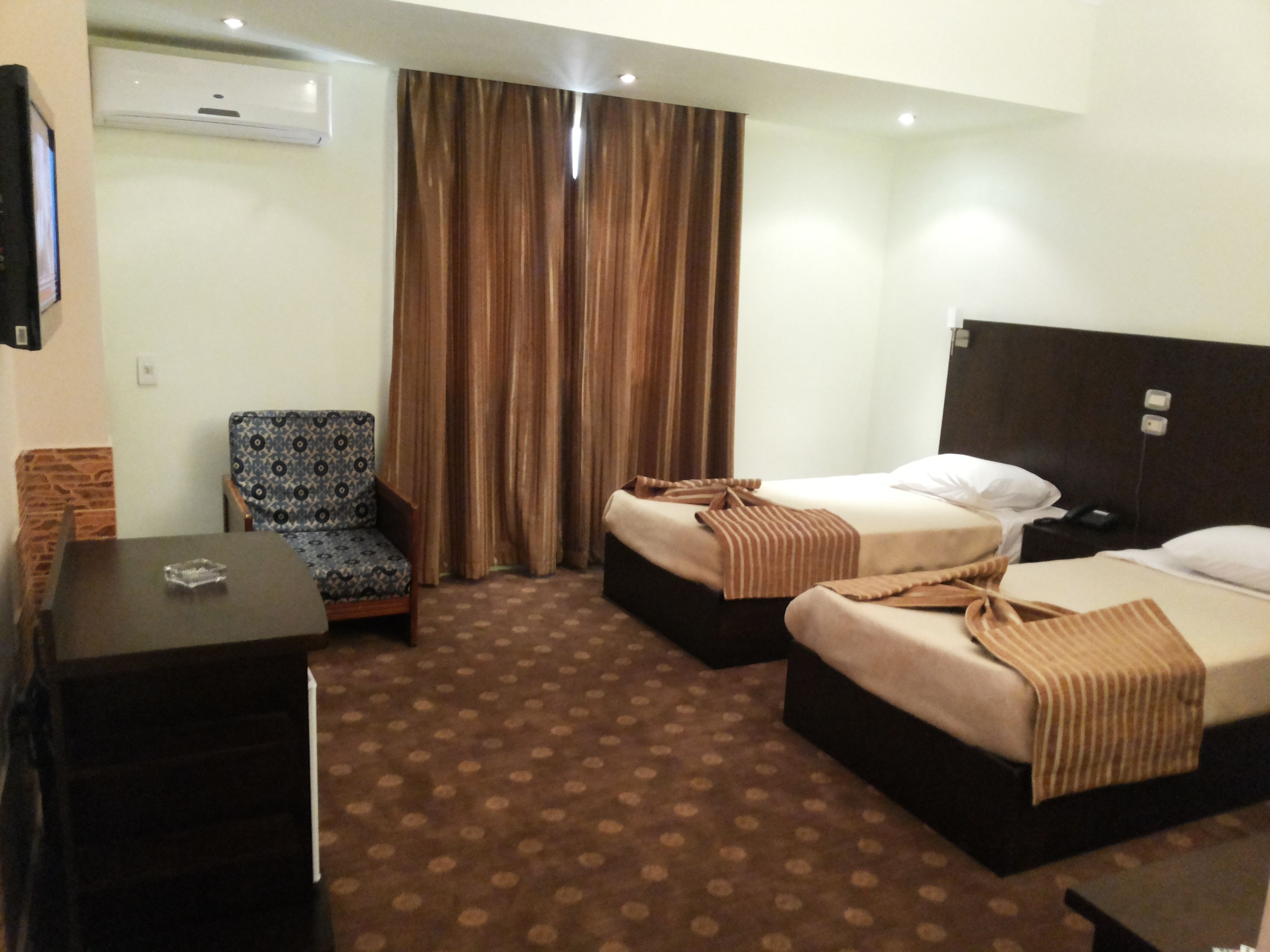 A hotel room with two beds, a small table, a chair, and a curtain.