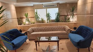 Un vestíbulo con un sofá color beige, dos sillones azules, un suelo con estampado de estrellas y plantas en macetas.