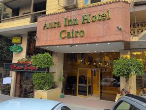 The exterior of Aura Inn Hotel in Cairo, featuring a prominent sign, a glass entrance, and potted plants. - Aura Inn Hotel Cairo (Giza)