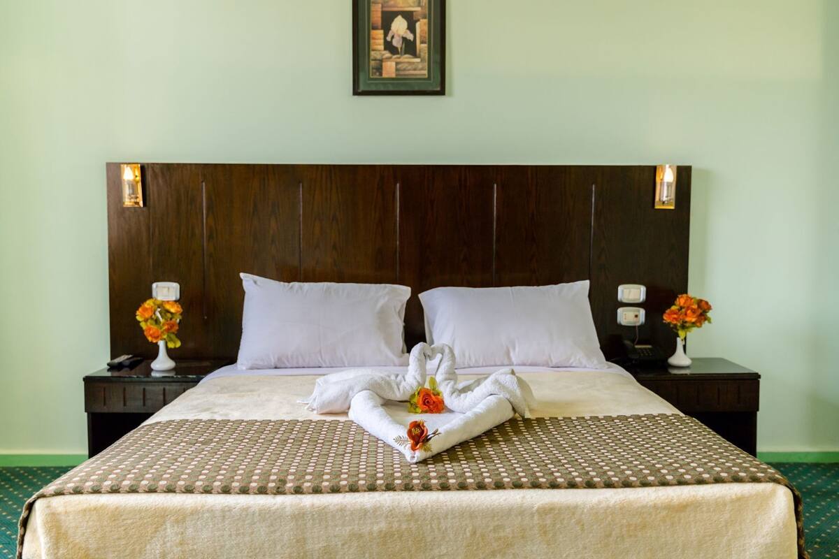 A hotel room with a large bed, two nightstands, a wooden headboard, and floral arrangements.