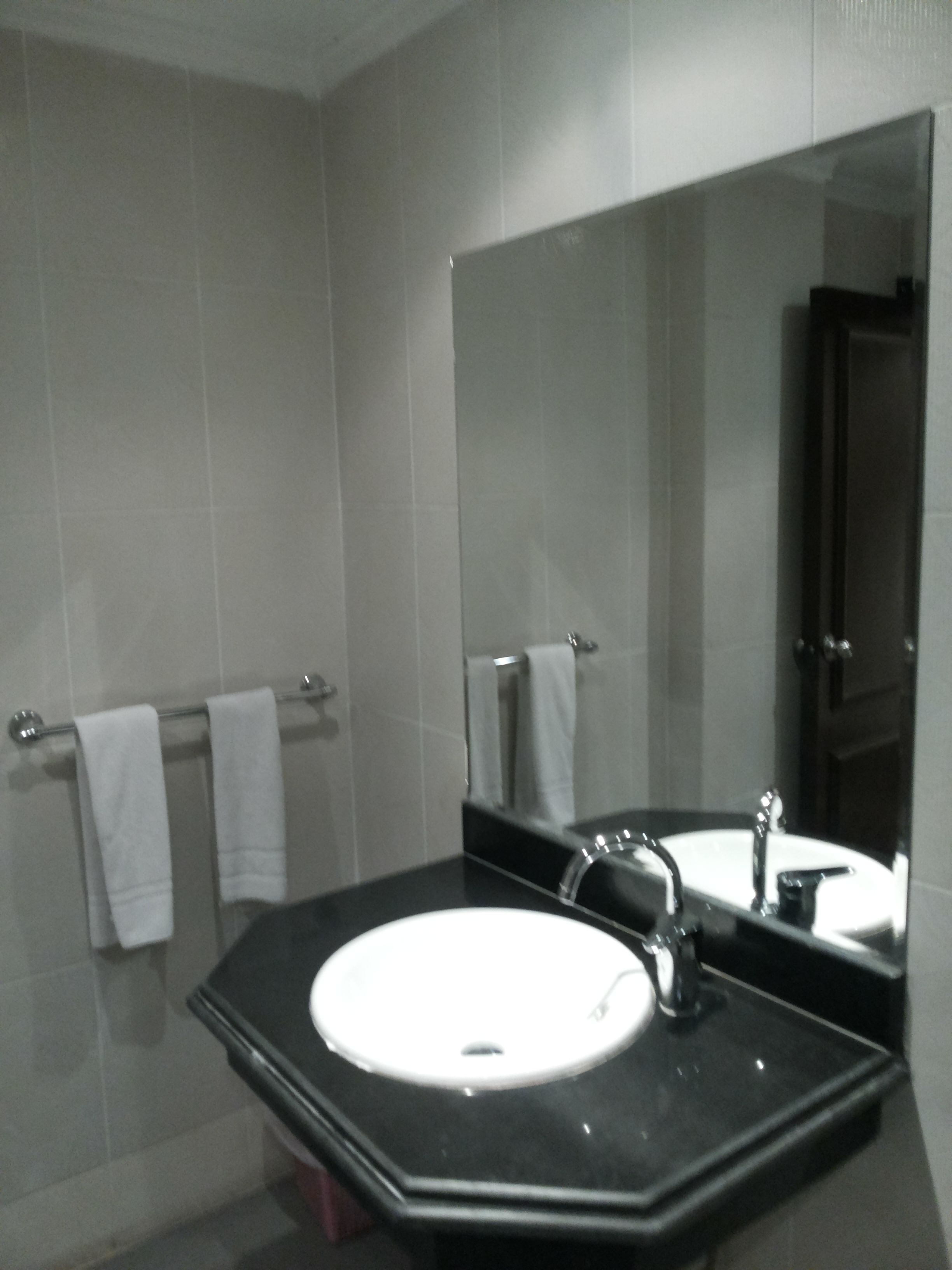Une salle de bain avec un lavabo blanc, un comptoir noir et un grand miroir. Deux serviettes blanches sont suspendues à un porte-serviettes.