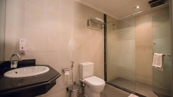 Een moderne badkamer met een douche met glazen wand, een wit wastafeltje en een toilet.