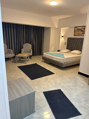 A modern hotel room with a bed, two armchairs, a small table, and a large window with curtains. - Aura Inn Hotel Cairo (Giza)