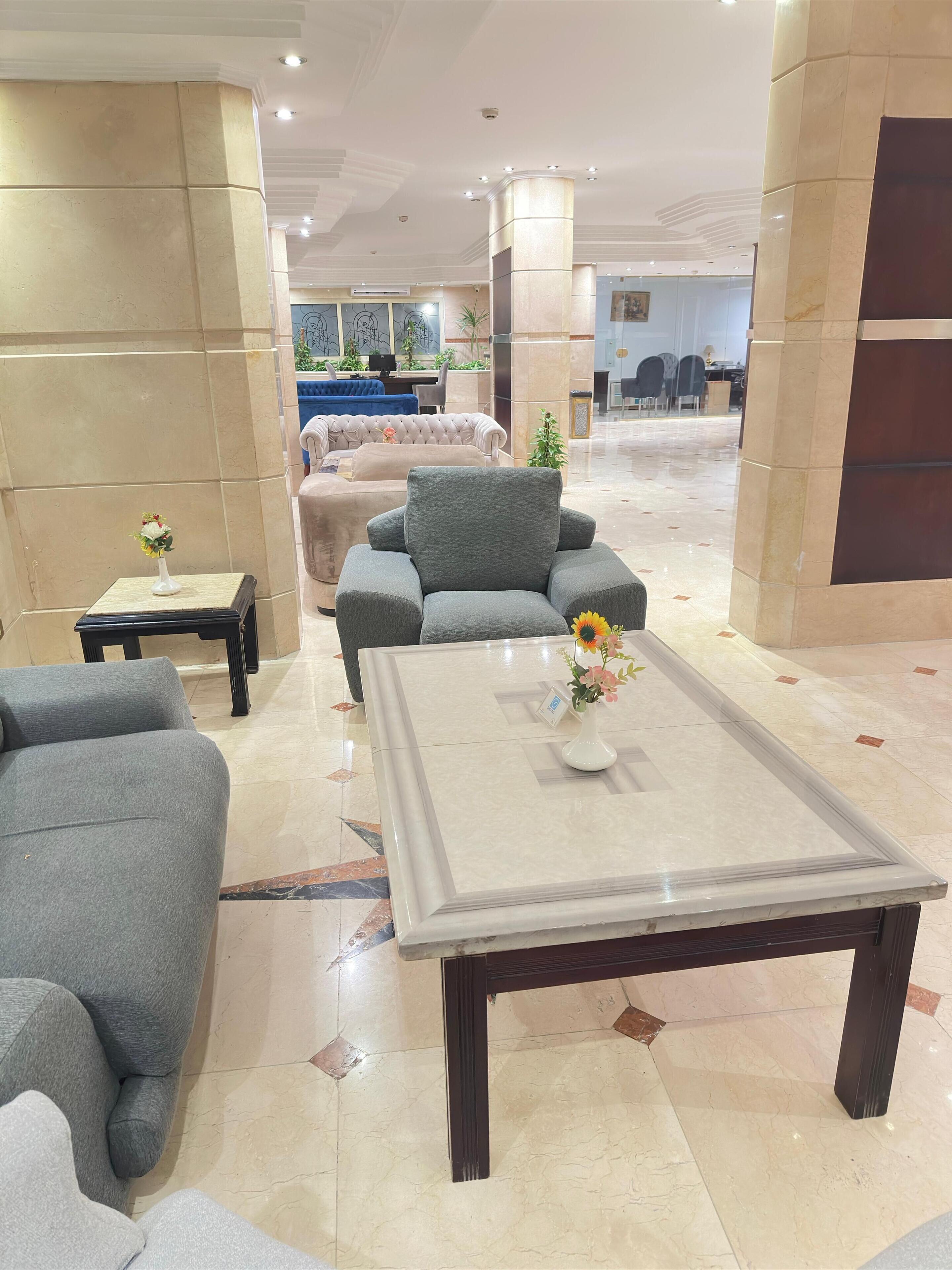 Een ruime lobby met een grote grijze bank, een bijpassende fauteuil en een salontafel met een bloemenvaas.
