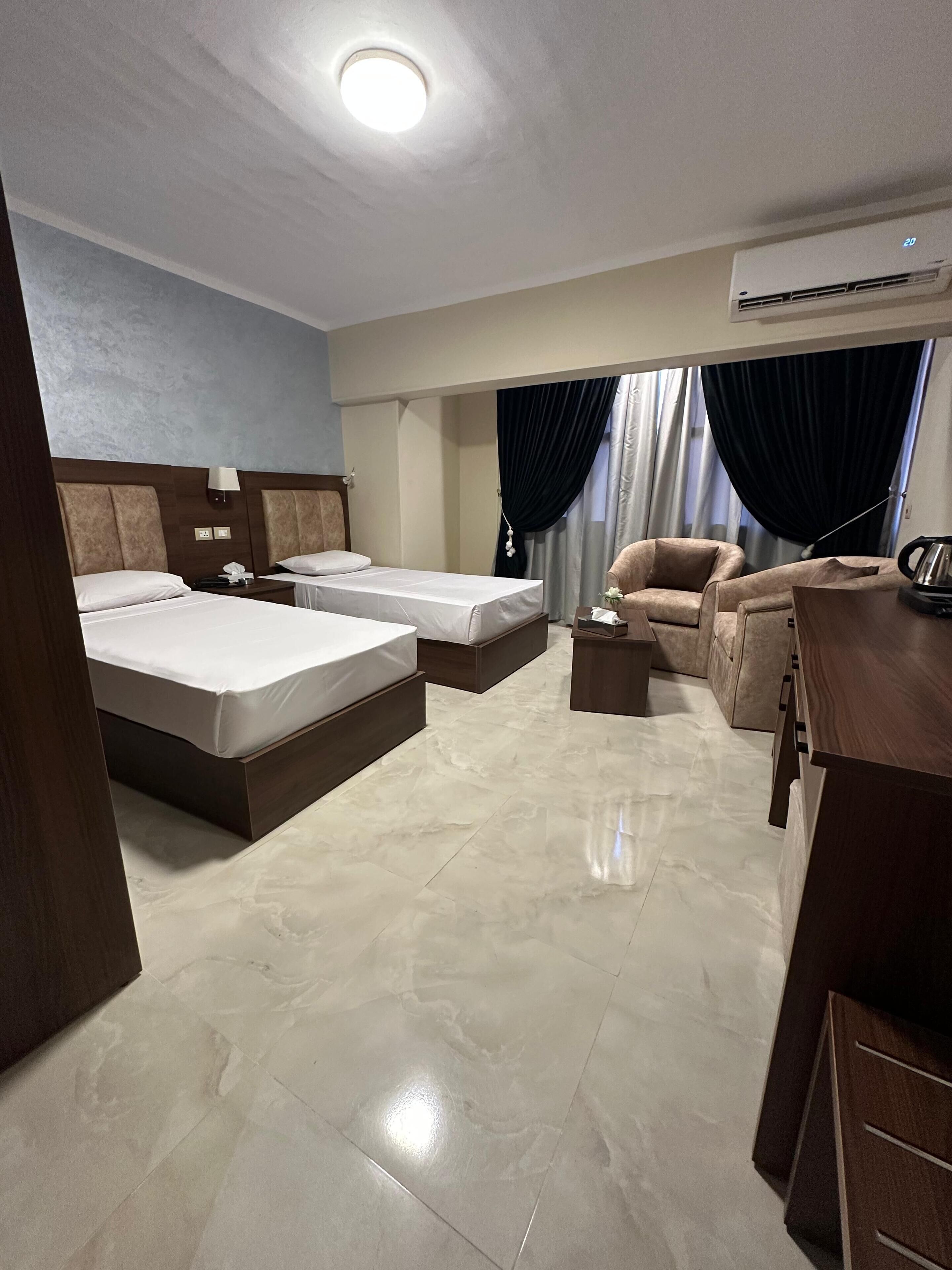 Une chambre d’hôtel avec deux lits, un canapé, un bureau et un luminaire au plafond.