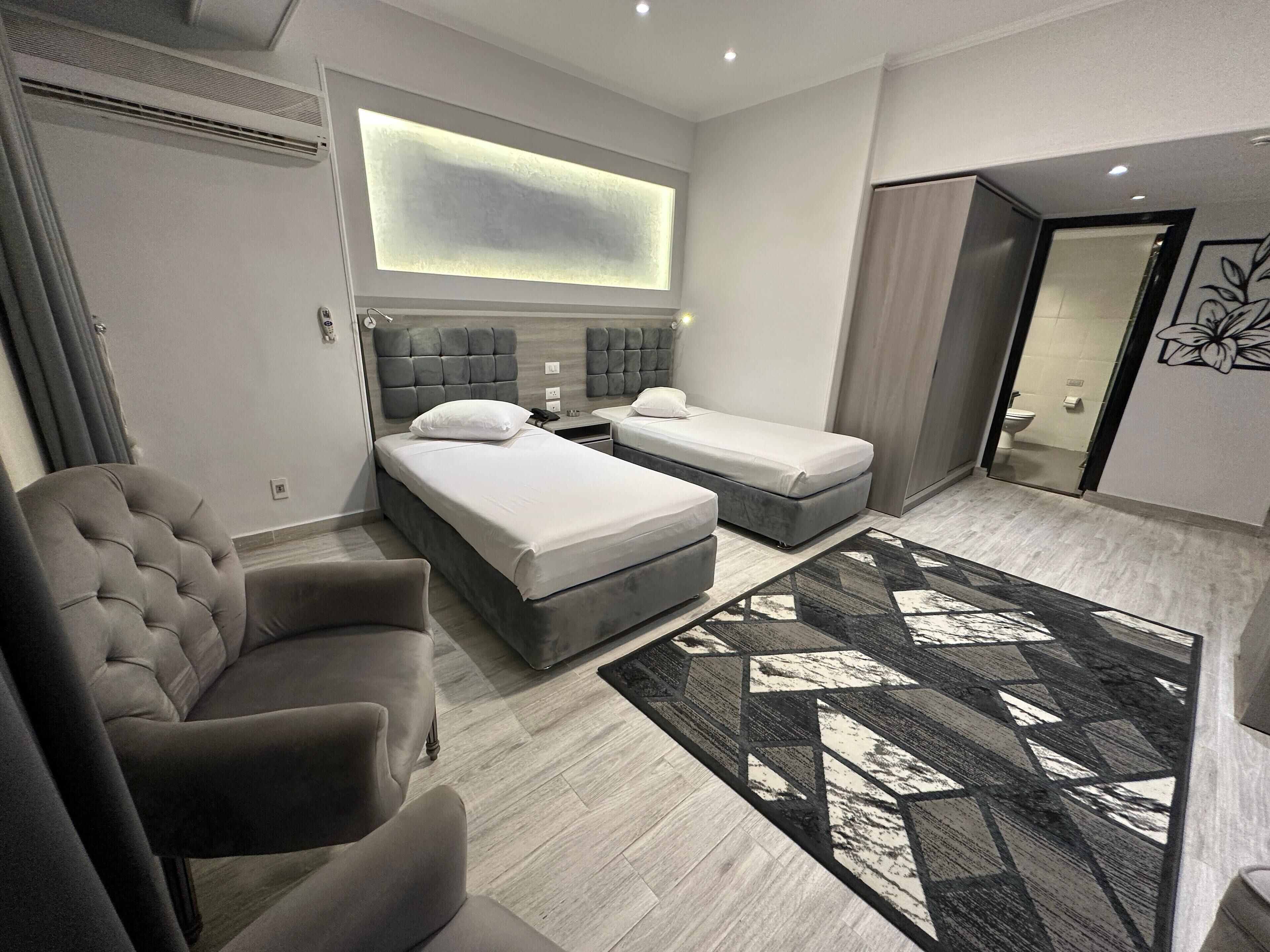 A modern hotel room with a large bed, a smaller bed, a sofa, and a decorative rug.