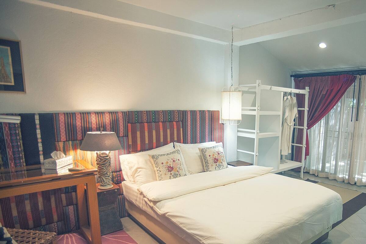 Un dormitorio con cama, mesita de noche, lámpara y ventana con cortinas.