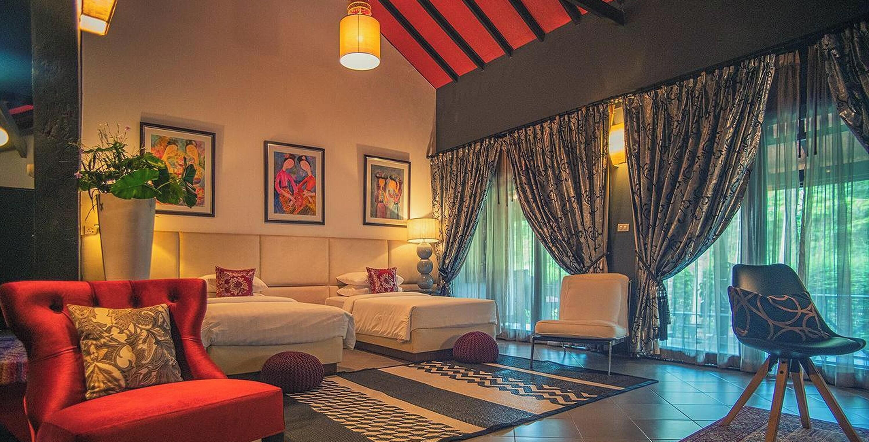 A hotel room with two beds, a red armchair, a white armchair, a patterned rug, and artwork on the walls.