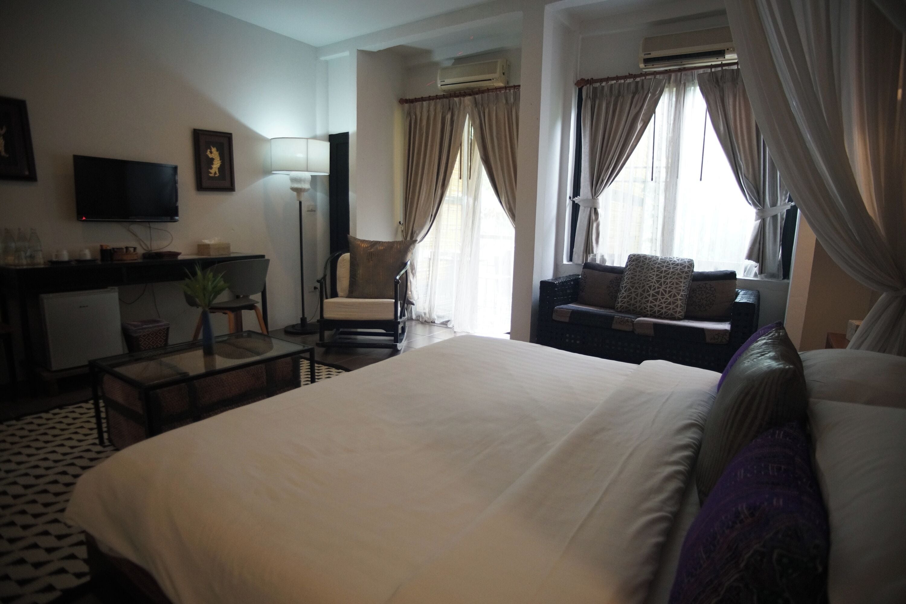 A hotel room with a bed, a sofa, a desk with a computer, a TV, and a window with curtains.