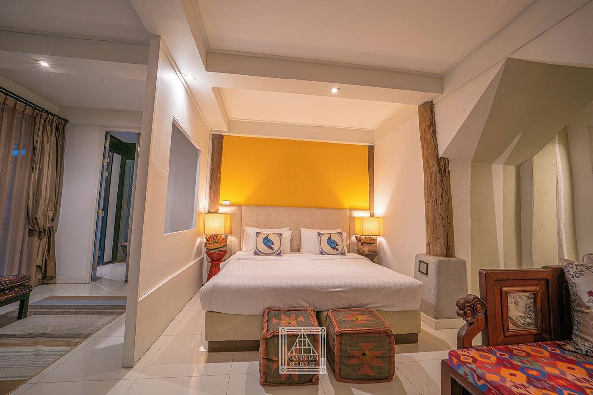 Habitación de hotel con una cama grande, lámparas de noche, cabecera de madera, un banco y una mesita.