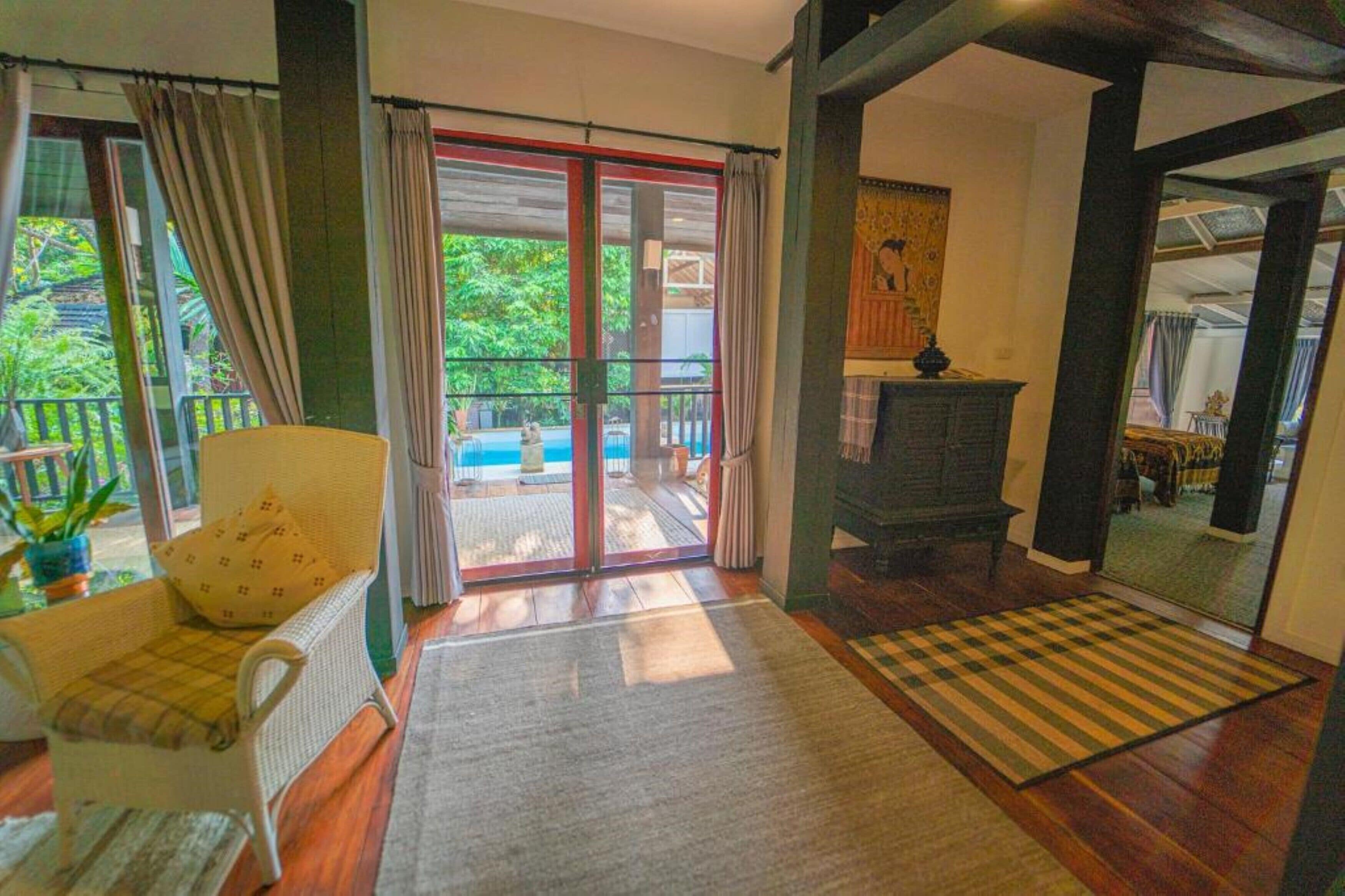 A room with a wooden floor, a sofa, a chair, a fireplace, and a view of a balcony with a pool.
