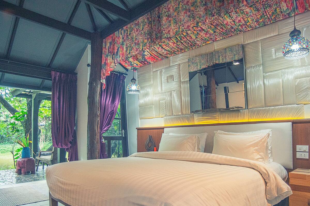 Un dormitorio con una cama grande, cabecera de madera y vista a zonas verdes.