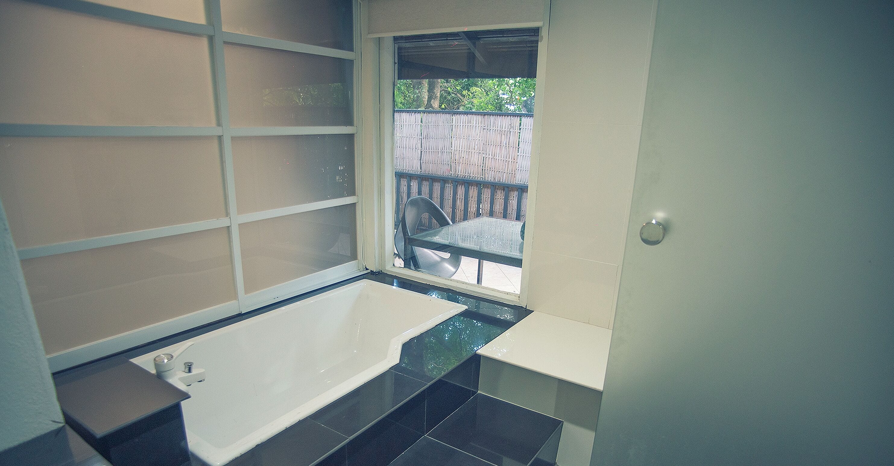 A bathroom with a bathtub, a window, and a view of a wooden deck.
