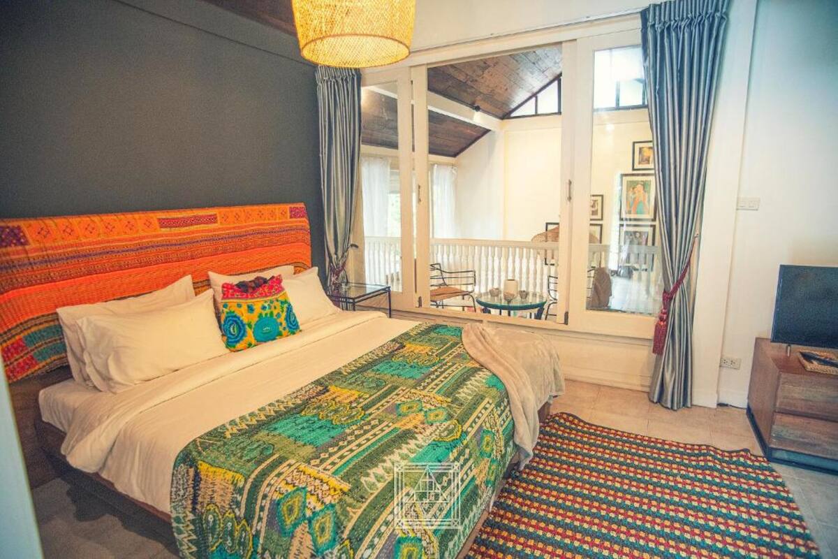 Un dormitorio con una cama grande, un cabecero colorido, vistas al balcón y una ventana con cortinas.