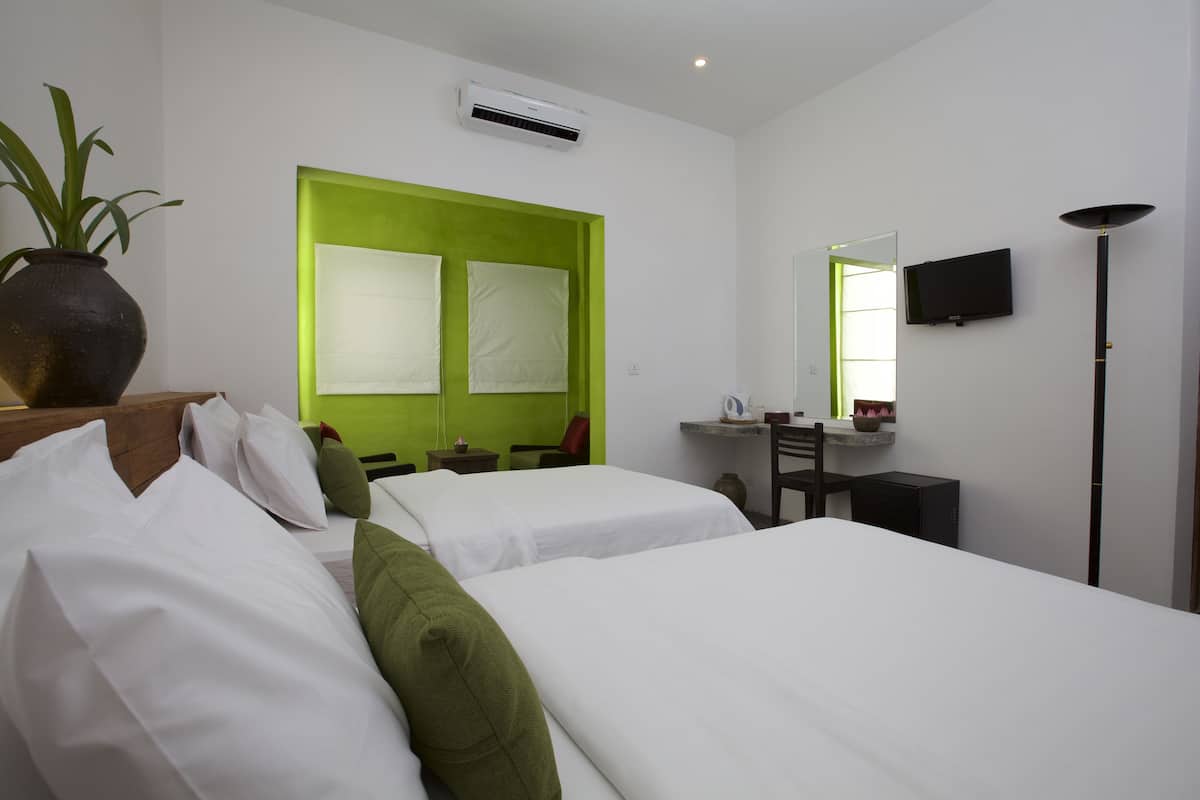 Ein Hotelzimmer mit zwei Betten, einem Schreibtisch, einem Sessel, einem Fernseher und einer Pflanze.