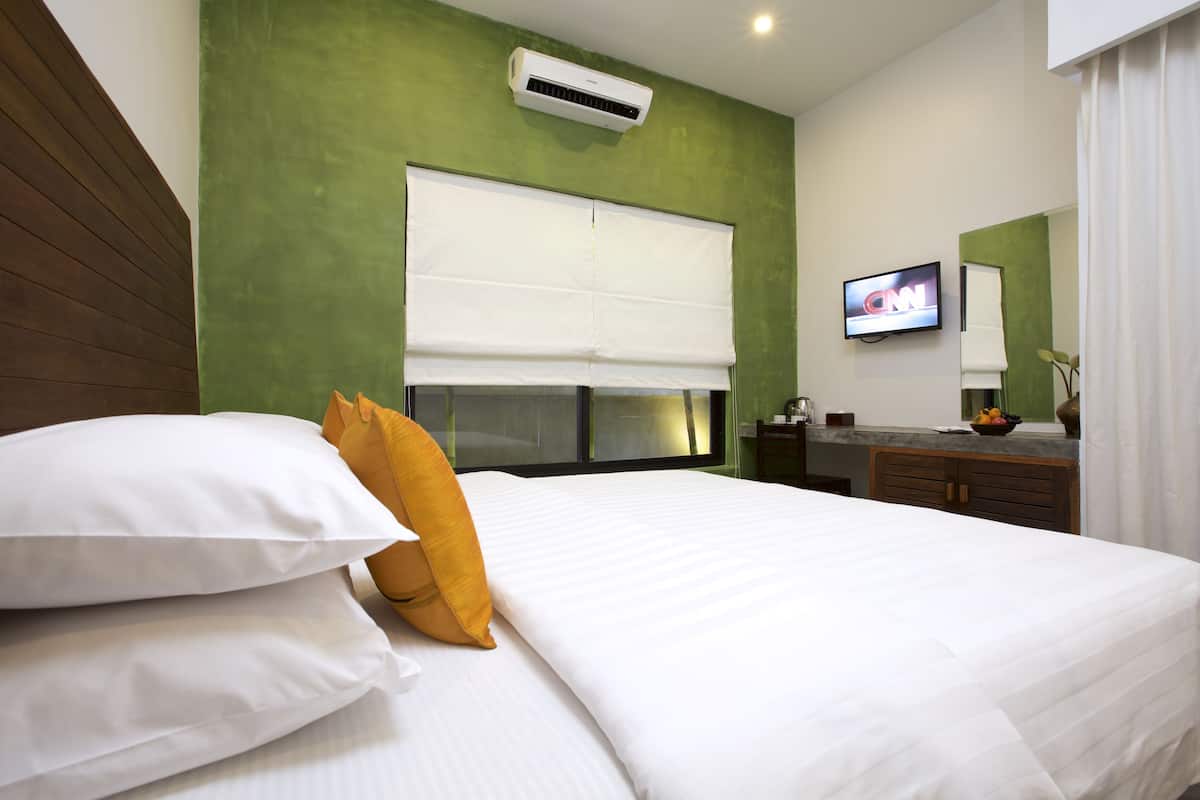 Ein Hotelzimmer mit Bett, Fernseher, Spiegel und einem Fenster mit Jalousien.