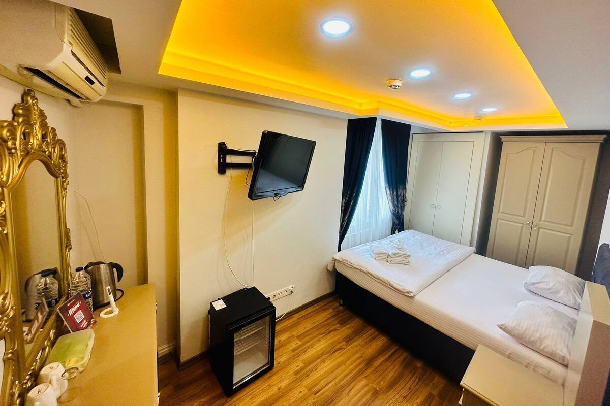 Una habitación de hotel con una cama, televisión montada, aire acondicionado, un calefactor pequeño y un espejo.