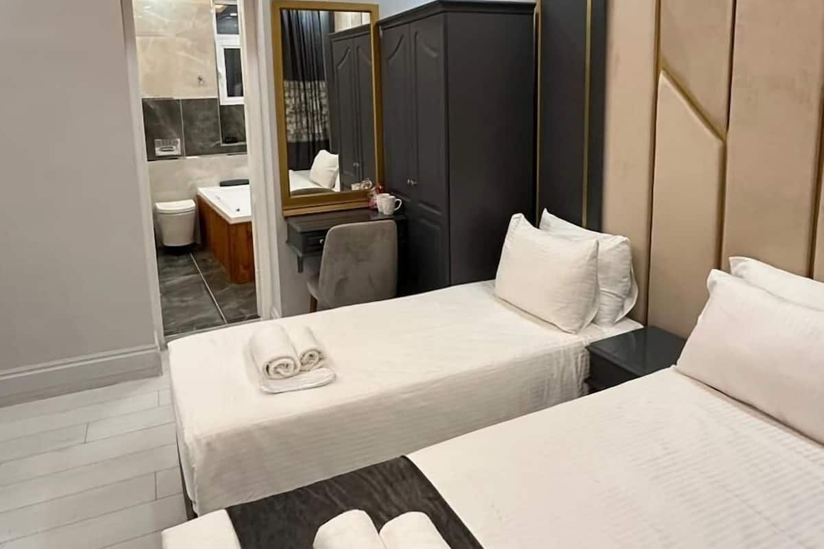 Habitación de hotel con dos camas, un escritorio, una silla y un baño visible a través de una puerta abierta.