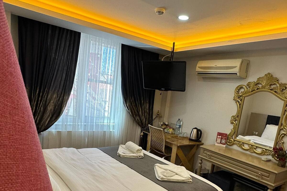 Habitación de hotel con una cama, un escritorio con espejo, un televisor y un equipo de aire acondicionado.