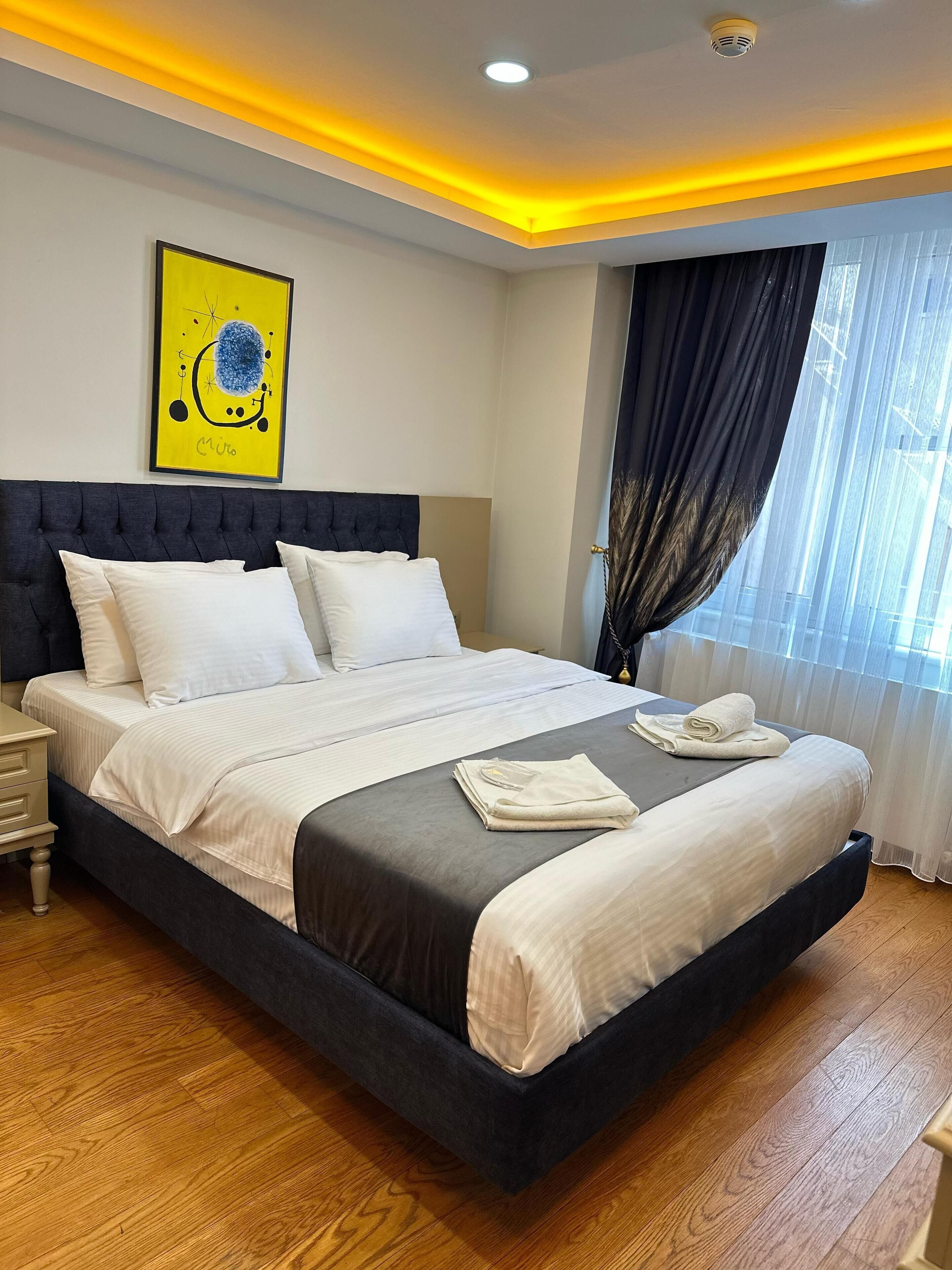 A modern bedroom with a large bed, a headboard, a bedside table, and a window with curtains.