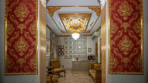A room with a chandelier, red and gold patterned walls, a marble floor, and a television on a cabinet. - Hotel Next2 (Istanbul)