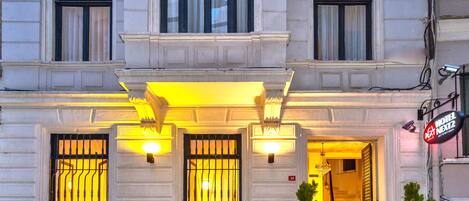 A hotel entrance with a red carpet, large windows with black bars, and a sign indicating the hotel name.