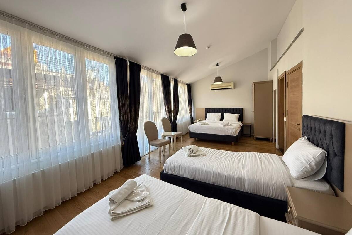 Habitación de hotel con dos camas, un escritorio, una silla y un ventanal con cortinas.