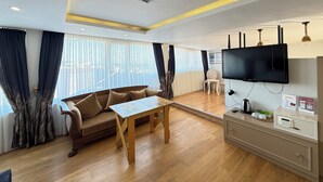 A modern living room with a sofa, wooden table, TV, and a view through large windows. - Hotel Next2 (Istanbul)
