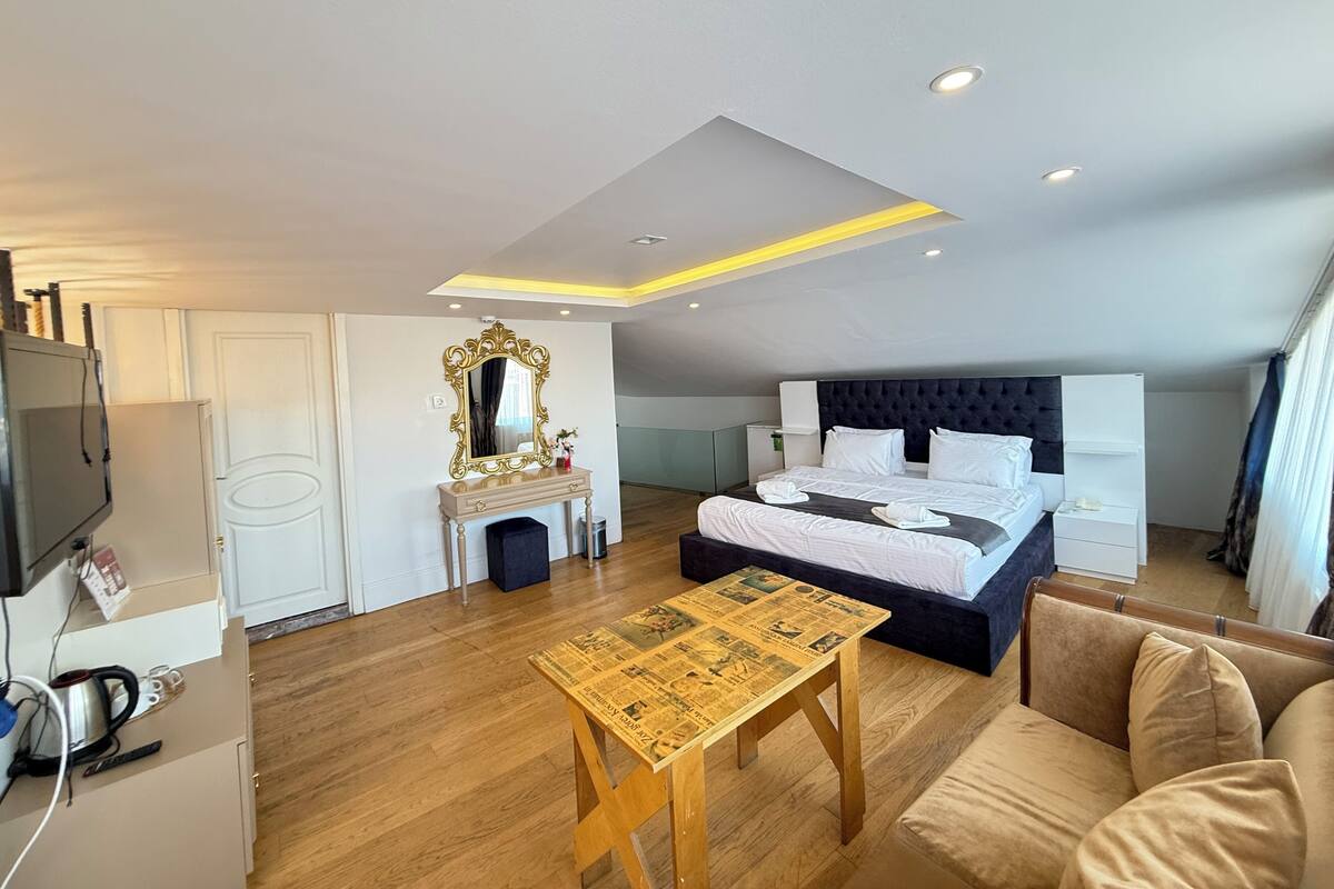 Una habitación de hotel moderna con cama, mesitas de noche, escritorio, espejo y televisión.