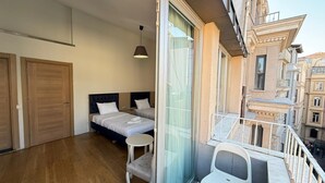 A bedroom with two beds, a small table, and a balcony with a chair. - Hotel Next2 (Istanbul)