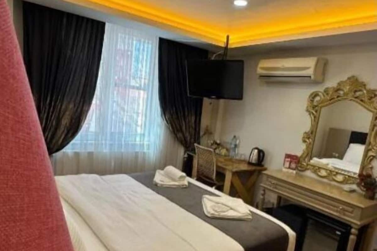 Ein Hotelzimmer mit einem Bett, einem Schreibtisch mit Spiegel, einem Flachbildfernseher und einer Klimaanlage.