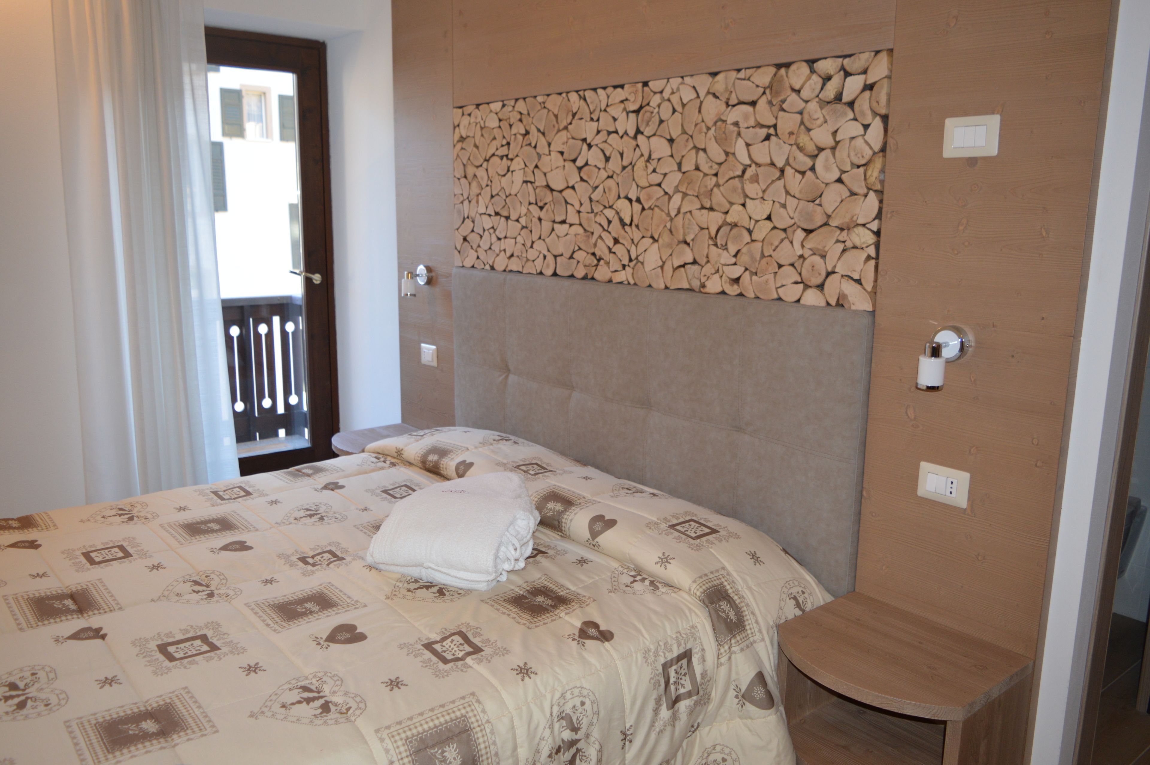 A bedroom with a bed, a wooden headboard, a small wooden stool, and a wall with a log pattern.