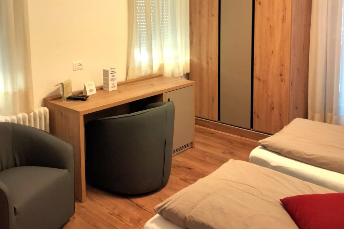 A hotel room with a wooden desk, a television mounted on the wall, a bed with two pillows, and a small seating area.