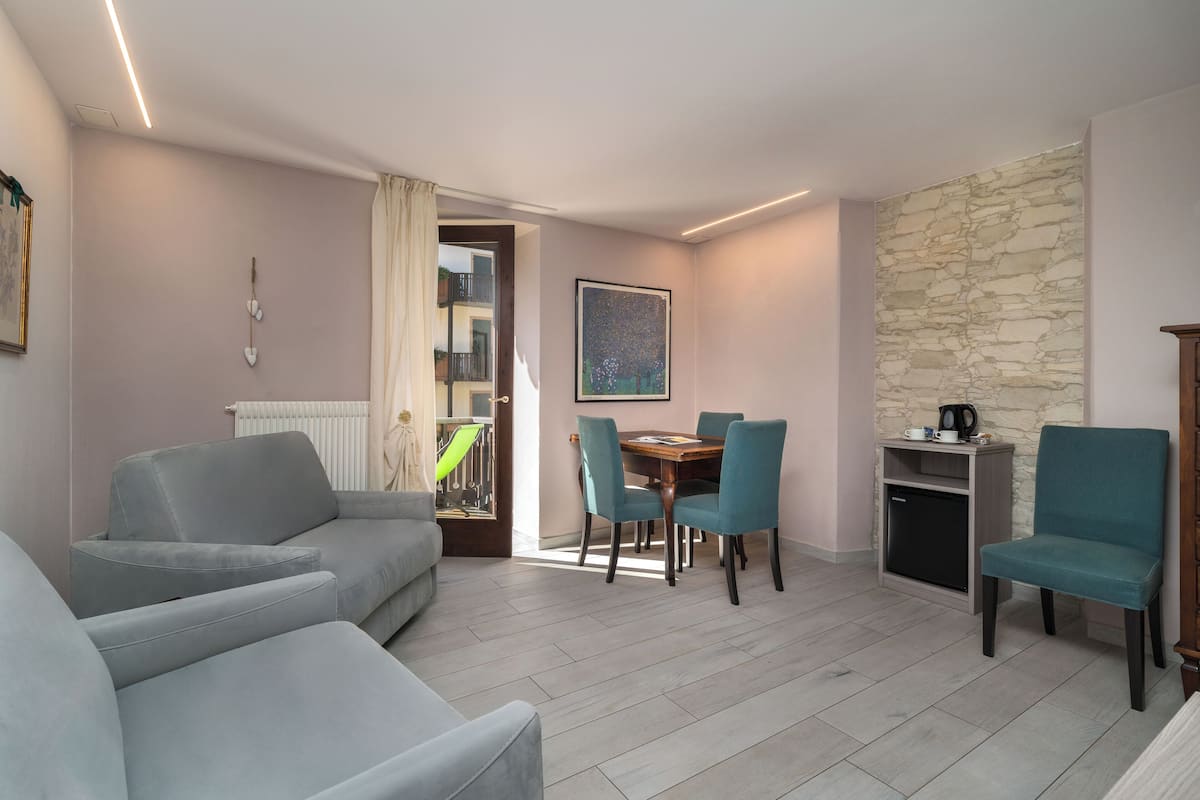 A modern living room with a grey sofa, teal chairs, a dining table, and a stone accent wall.
