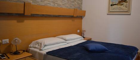 A hotel room with a wooden headboard, a bed with white and blue bedding, a nightstand with a lamp, and a painting on the wall.