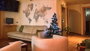 A living room with a world map on the wall, a Christmas tree, a sofa, and a television. - Hotel Wanda (Pinzolo)
