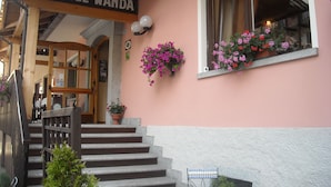 A hotel entrance with a wooden staircase, a sign reading "HOTEL WANDA", and flower boxes on the windows. - Hotel Wanda (Pinzolo)
