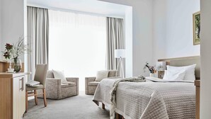 Una habitación de hotel con una cama, dos sillones, un escritorio y una lámpara.