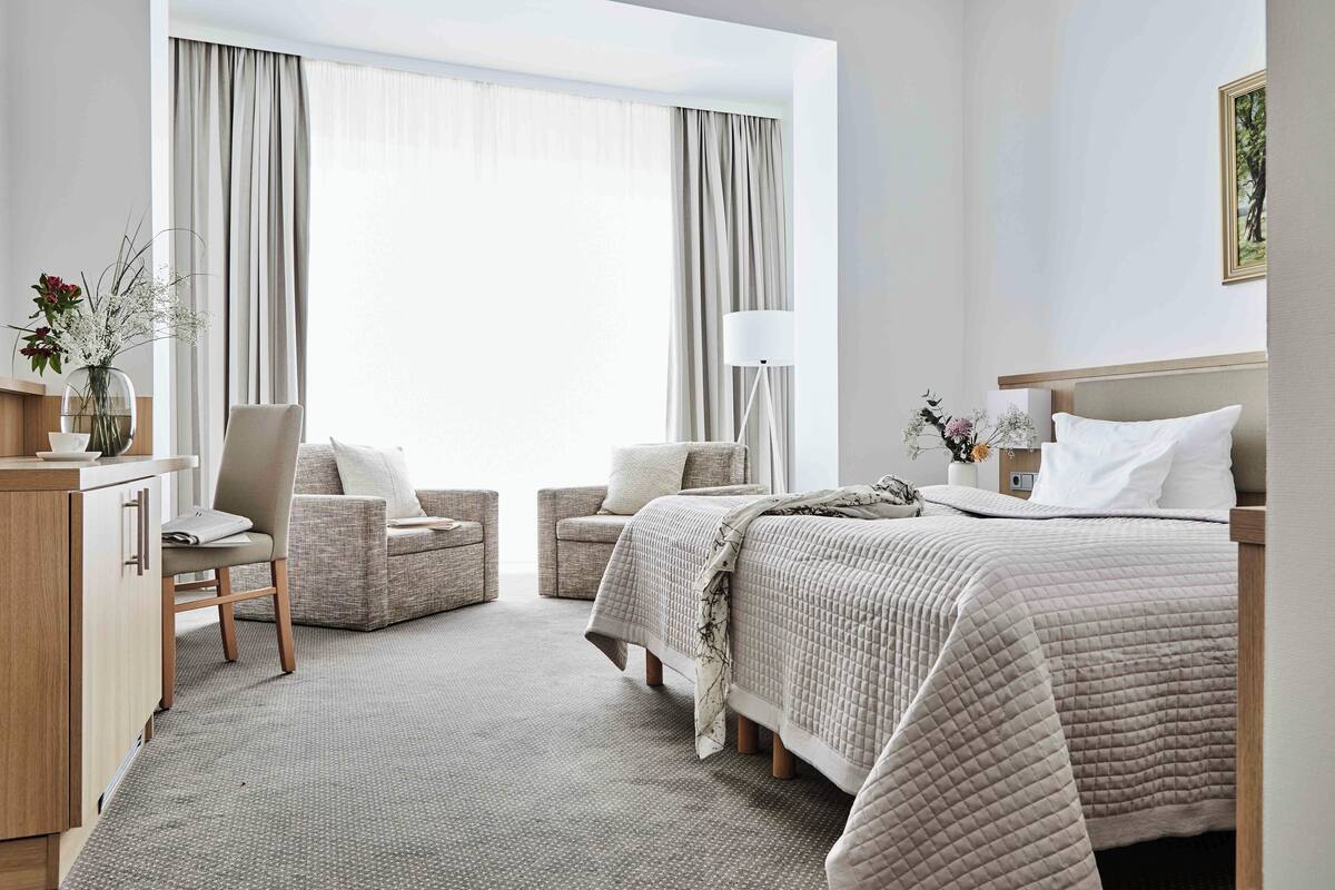 A hotel room with a bed, two armchairs, a desk, and a lamp.