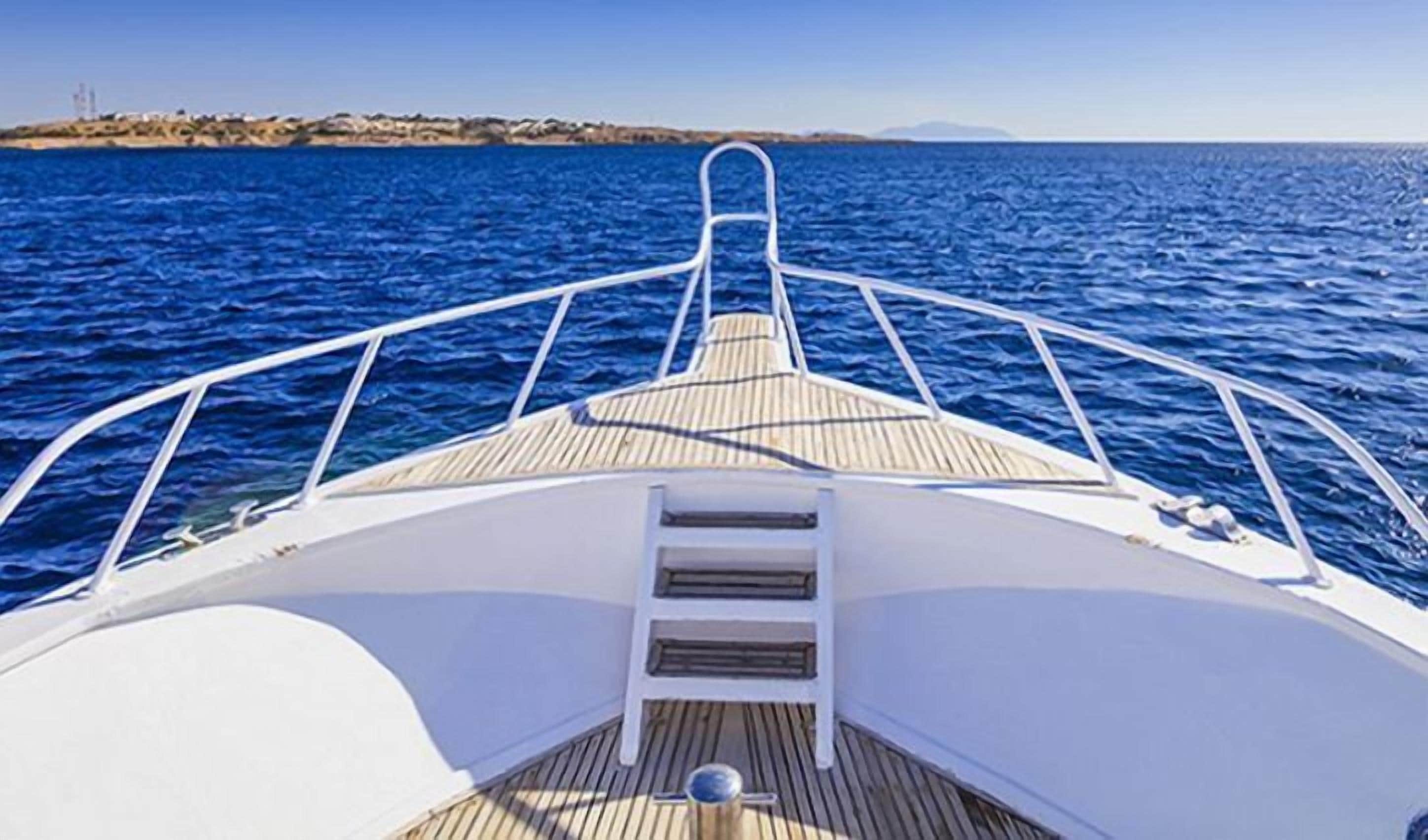 The deck of a boat with a wooden floor, metal railings, and a view of the sea and distant land.